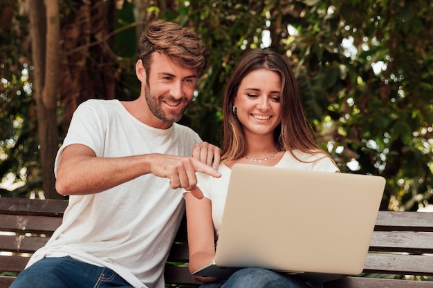 Amici che si siedono su una panchina con un computer portatile