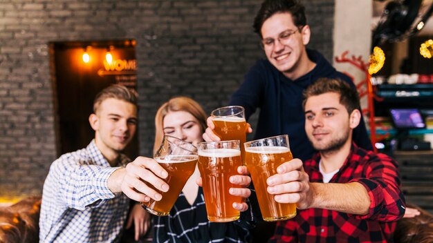 Amici che tintinnano i vetri con birra in pub