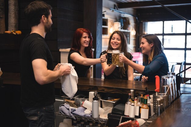 Amici che tostano con bicchieri di birra al bancone del bar