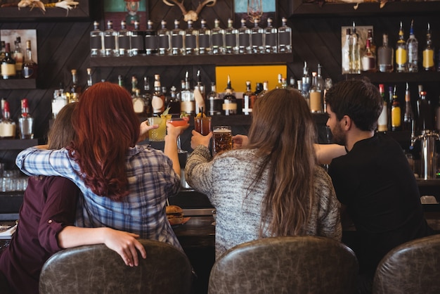 Amici che tostano con birra e bicchieri da cocktail al bar