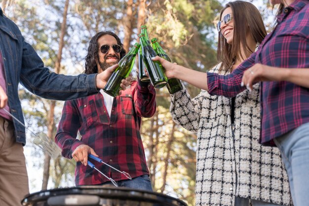 Amici che tostano con la birra all'aperto sopra il barbecue