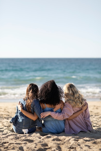 Amici del colpo pieno che si siedono insieme alla spiaggia