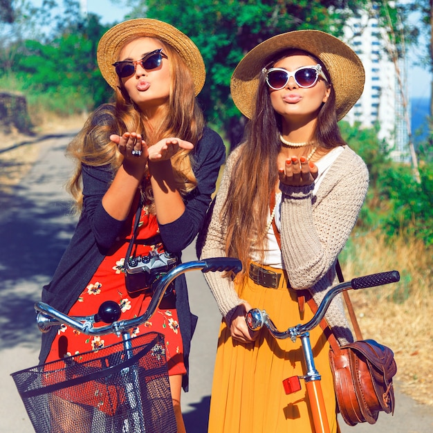Amici delle donne hipster che soffia un bacio. Divertirsi insieme passeggiando con le biciclette nel parco vicino al mare.