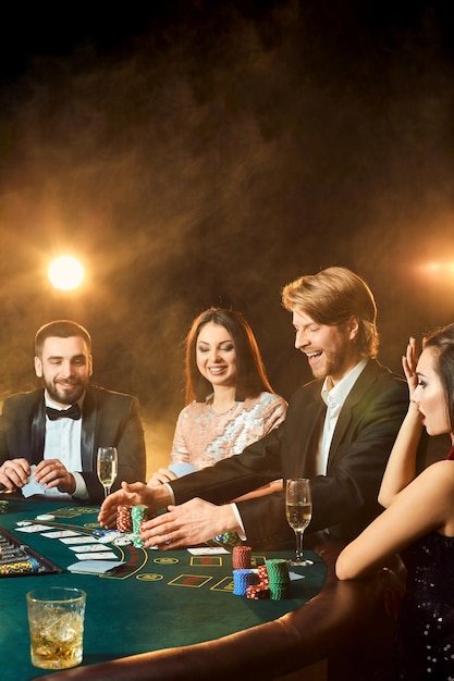 Amici di classe superiore che giocano al casinò. Due uomini in completo e due giovani donne in abito. Fumo. Casinò. Poker