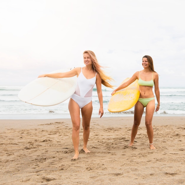 Amici di sesso femminile in spiaggia tenendo le tavole da surf