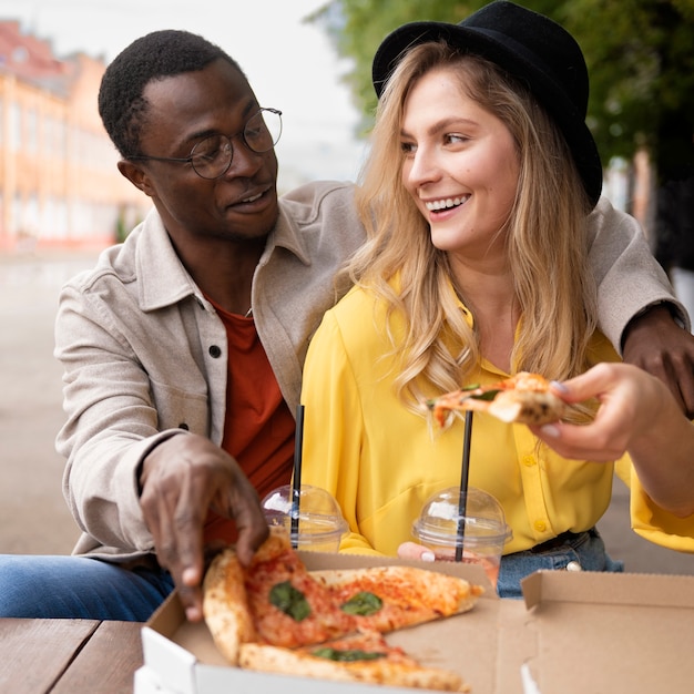 Amici di smiley di vista frontale che mangiano pizza all'aperto