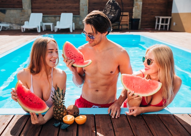 Amici di vista frontale che mangiano anguria in piscina