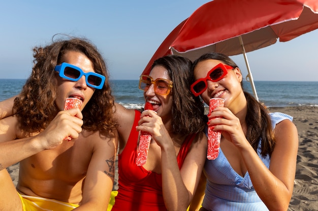 Amici di vista frontale che mangiano il gelato sulla spiaggia