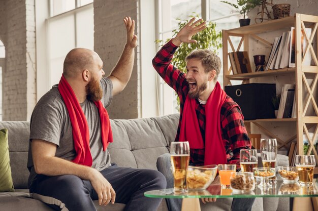 Amici emozionati e felici che guardano basket, calcio, calcio, partita di tennis, campionato sul divano di casa.