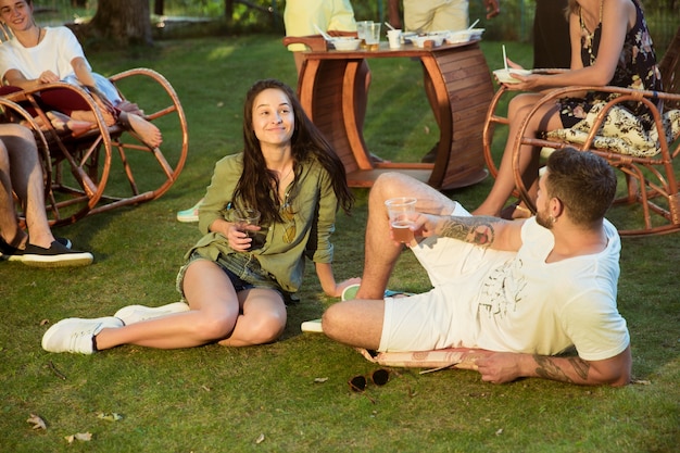 Amici felici che mangiano e bevono birre alla cena barbecue sul tramonto