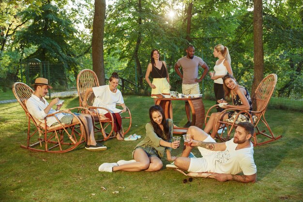 Amici felici che mangiano e bevono birre alla cena barbecue sul tramonto