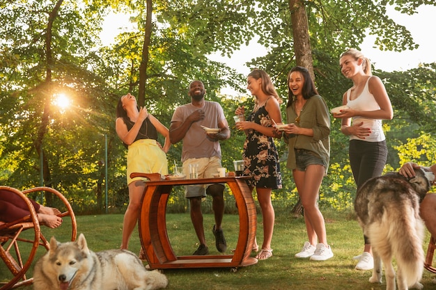 Amici felici che mangiano e bevono birre alla cena barbecue sull'ora del tramonto