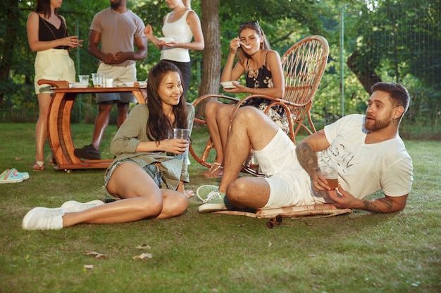 Amici felici che mangiano e bevono birre alla cena barbecue sull'ora del tramonto