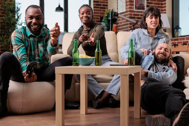 Amici felici che si divertono a giocare a strategia di videogiochi alla festa in casa con bottiglie di birra e snack. Gruppo di amici che celebrano la riunione dell'hangout mentre giocano sulla console TV.