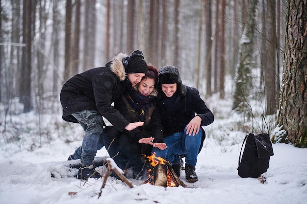 Amici felici che si scaldano accanto a un falò nella fredda foresta innevata