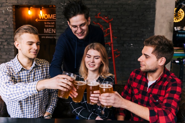 Amici felici che tintinnano i bicchieri di birra nel ristorante