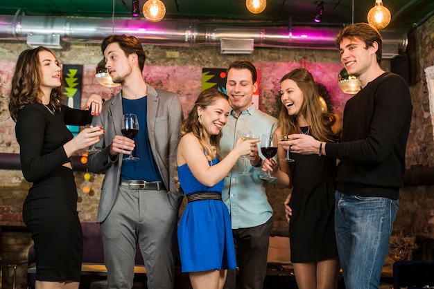 Amici felici di sesso maschile e femminile, bere e tostare cocktail in un bar