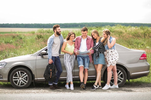 Amici felici guardando la mappa in piedi vicino l&#39;auto