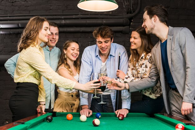 Amici felici maschi e femminili che tostano vino in club sopra la tavola di snooker in club