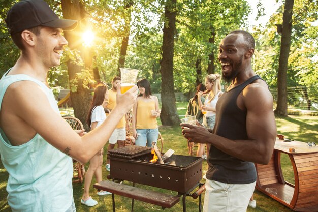 Amici felici stanno avendo birra e barbecue party in giornata di sole