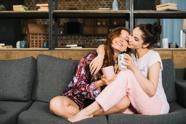 Amici femminili amichevoli che si siedono sul sofà con la tazza di caffè