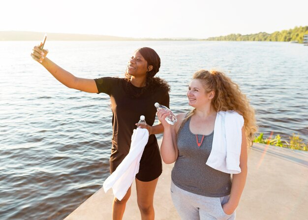 Amici femminili che prendono selfie insieme mentre si esercitano in riva al lago