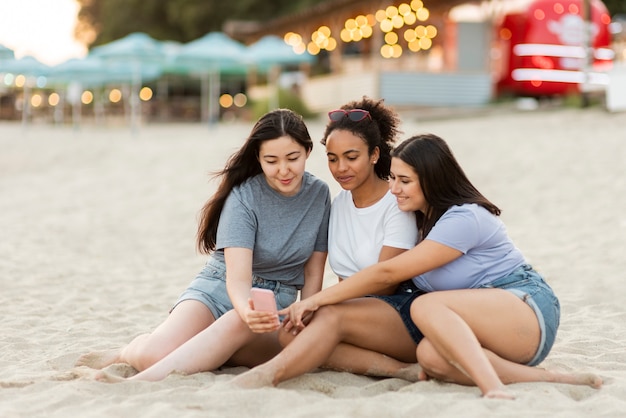 Amici femminili con lo smartphone che si siede sulla spiaggia