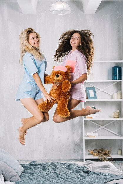 Amici femminili felici che saltano sopra il letto con il giocattolo molle