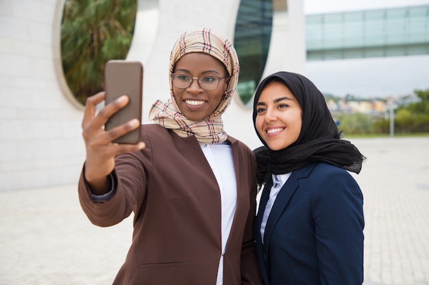 Amici femminili felici dell'ufficio che prendono selfie fuori