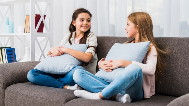 Amici femminili sorridenti che si siedono sul sofà con l&#39;ammortizzatore che guarda l&#39;un l&#39;altro