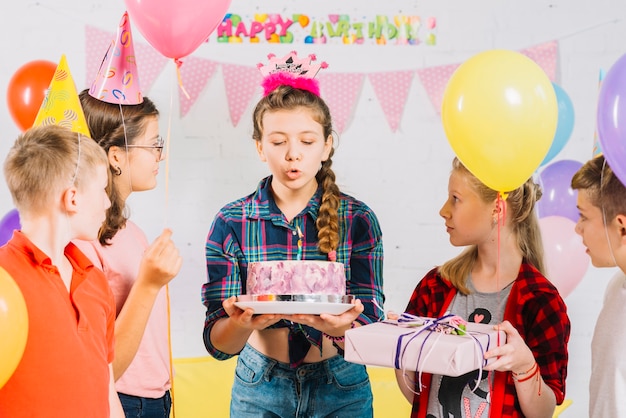 Amici guardando ragazza con torta di compleanno soffiando la candela