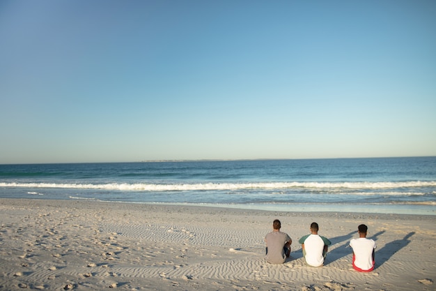 Amici maschi che si rilassano insieme sulla spiaggia