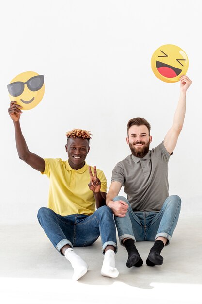 Amici maschi di copia-spazio che si siedono sul pavimento e che tengono emoji