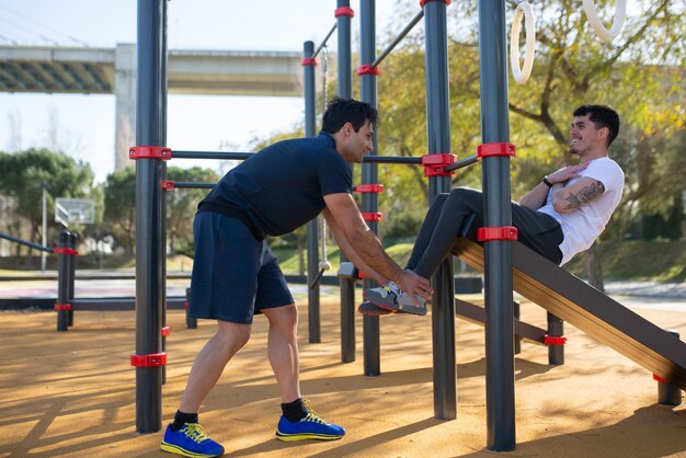 Amici maschi felici che si allenano in una giornata di sole. Due uomini in abiti sportivi su un campo sportivo all'aperto, che si aiutano a vicenda. Sport, salute, concetto di allenamento