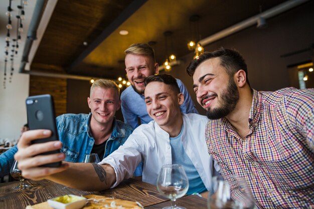 Amici maschii sorridenti che parlano autoritratto sul cellulare nel ristorante