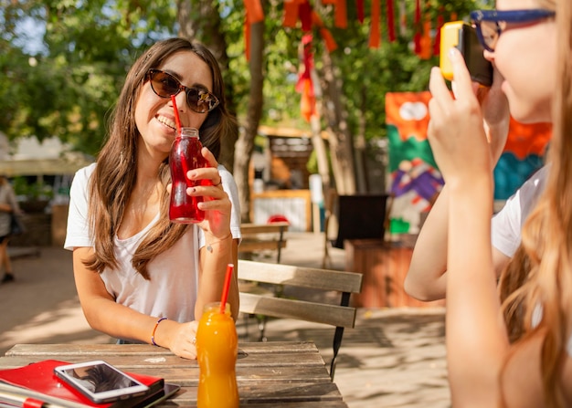 Amici nel parco che tengono le bottiglie di succo fresco e scattare foto