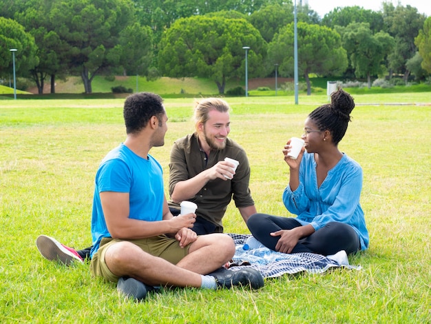 Amici sorridenti che bevono dalle tazze di carta in parco