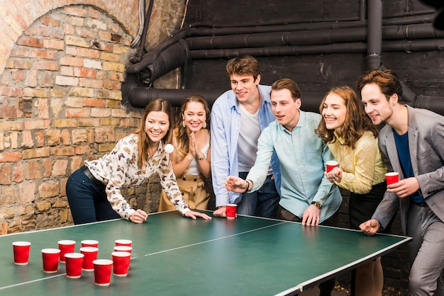 Amici sorridenti che giocano il pong della birra sulla tavola nella barra