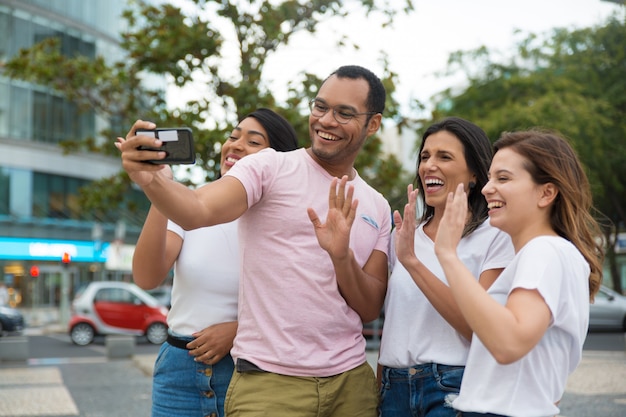 Amici sorridenti che ondeggiano al telefono della macchina fotografica