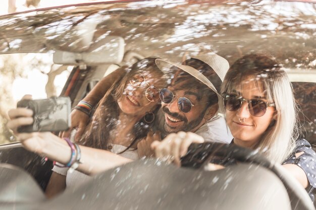 Amici sorridenti che viaggiano in auto prendendo selfie attraverso il cellulare