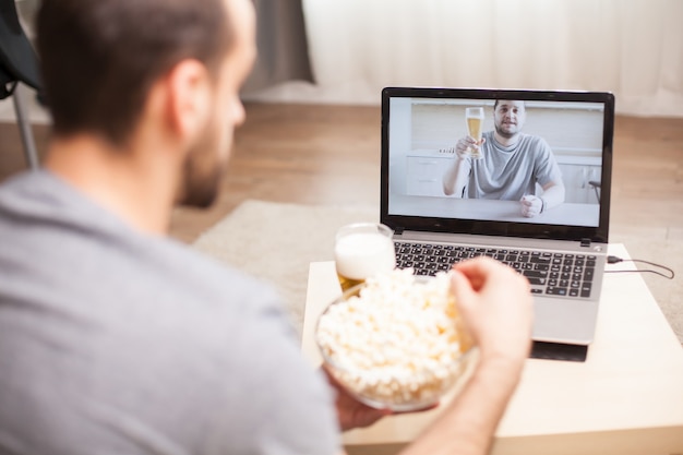 Amico che beve birra e mangia popcorn durante una videochiamata durante la quarantena.