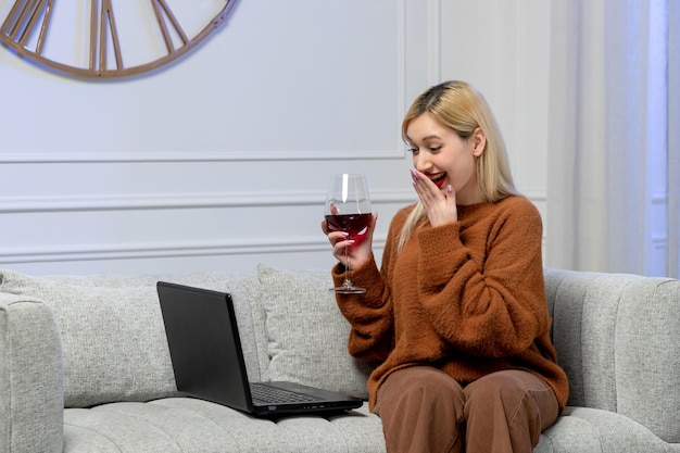 Amore virtuale carina giovane ragazza bionda in maglione accogliente sulla data di distanza che copre la bocca con il vino