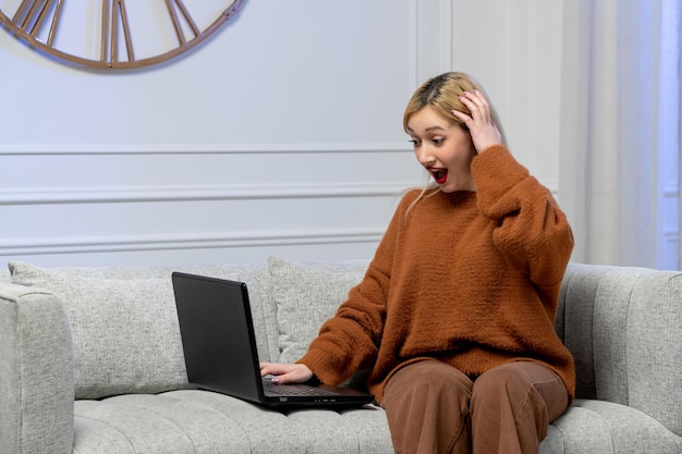 Amore virtuale carina giovane ragazza bionda in un maglione accogliente sulla data del computer a distanza che tiene la testa