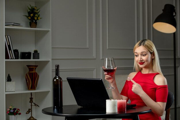 Amore virtuale ragazza bionda carina in abito rosso in data a distanza con vino che punta al bicchiere di vino