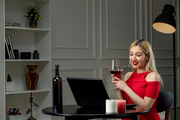 Amore virtuale ragazza bionda carina in abito rosso in un appuntamento a distanza con vino che beve vino