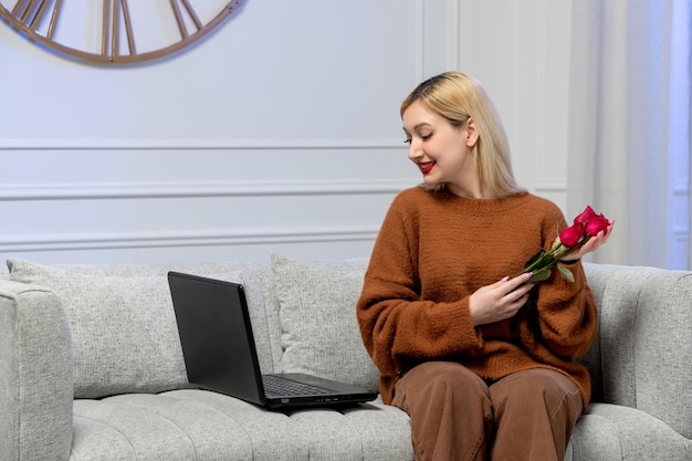 Amore virtuale ragazza bionda carina in maglione accogliente su computer a distanza data con fiori rossi