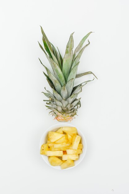 Ananas affettato in una ciotola bianca sulla vista bianca e superiore.