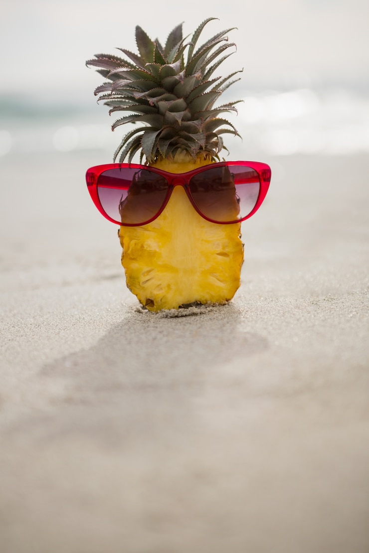 Foto gratuito ananas dimezzato e un occhiale da sole conservati sulla sabbia