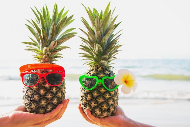 Ananas freschi adorabili delle coppie che mettono i vetri in mani turistiche con l'onda del mare - amore felice e divertimento con il concetto sano di vacanza