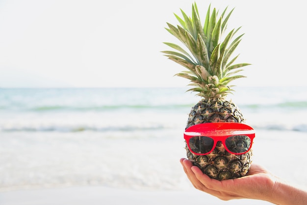 Ananas fresco adorabile che mette i vetri in mani turistiche con l&#39;onda del mare - divertimento felice con il concetto sano di vacanza